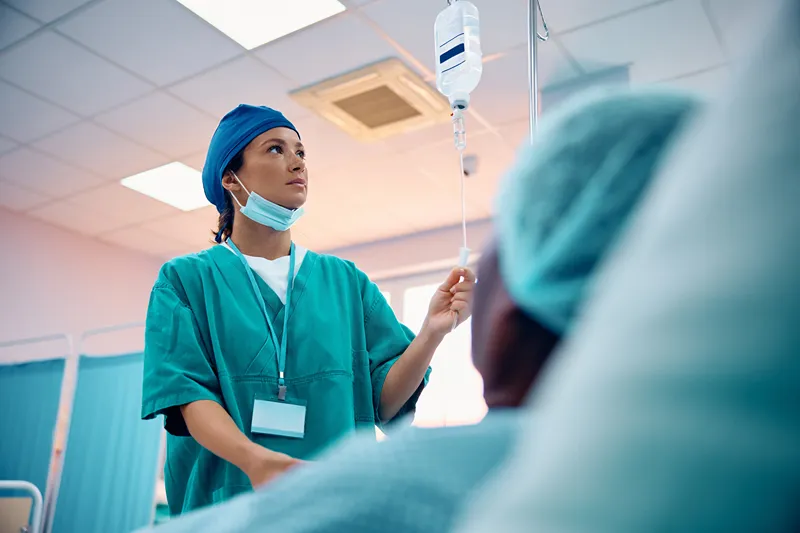 A nurse checking on an IV drip at a patien's bedside