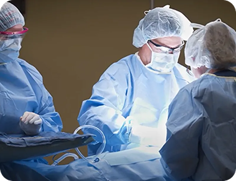 Three medical professionals in surgical scrubs, masks, and caps performing surgery in an operating room.