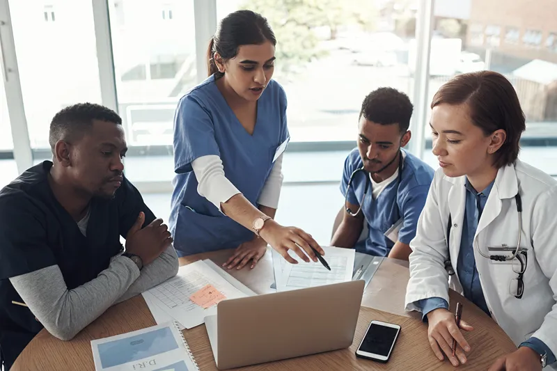 A group of medical professionals gathered around a table looking at a laptop