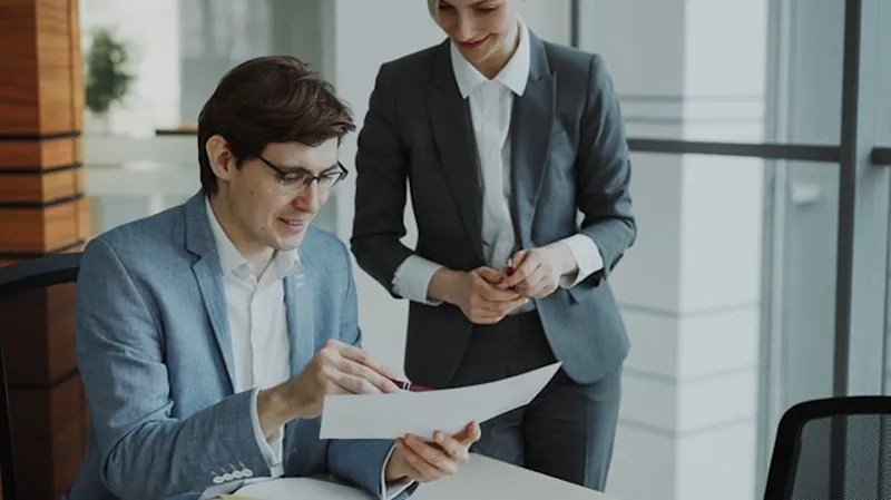A man going over the details of a piece of paper as a woman stands over their shoulder