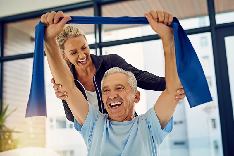 Smiling senior man performs resistance band exercises with a female physical therapist for medical rehabilitation