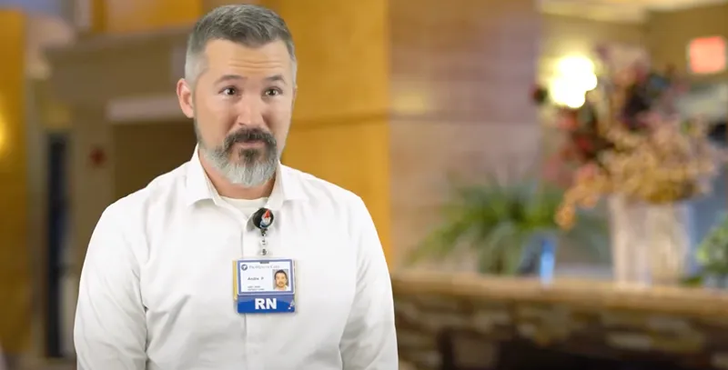 Registered nurse standing in hospital lobby wearing ID badge and white shirt