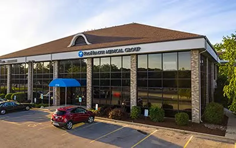 Exterior of ProHealth Medical Group Clinic in Delafield with large windows, a blue awning, and a parking lot.