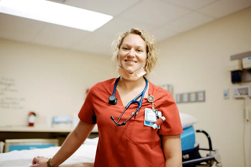 A photo of a medical professional in orange scrubs looking towards the camera