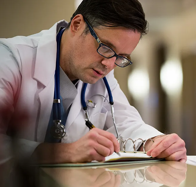 A photo of a medical professional hunched over writing on a piece of paper