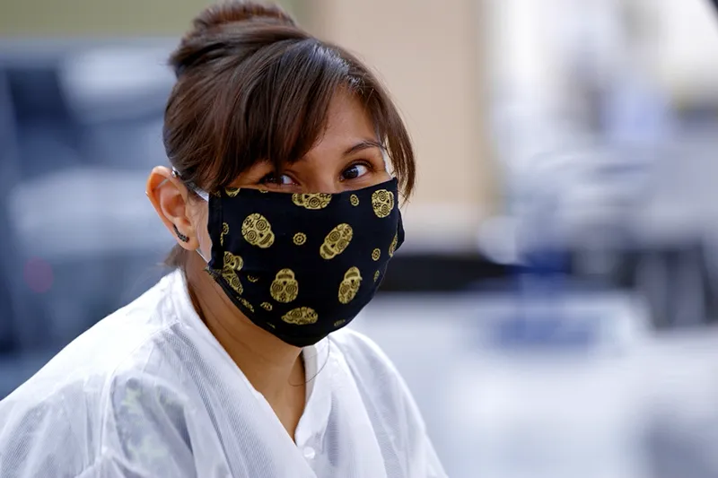 A closeup photo of a woman wearing a medical face mask looking into the camera