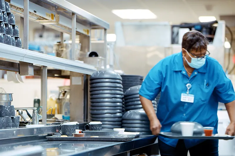A photo of a person carrying a tray of food in a industrial kitchen setting