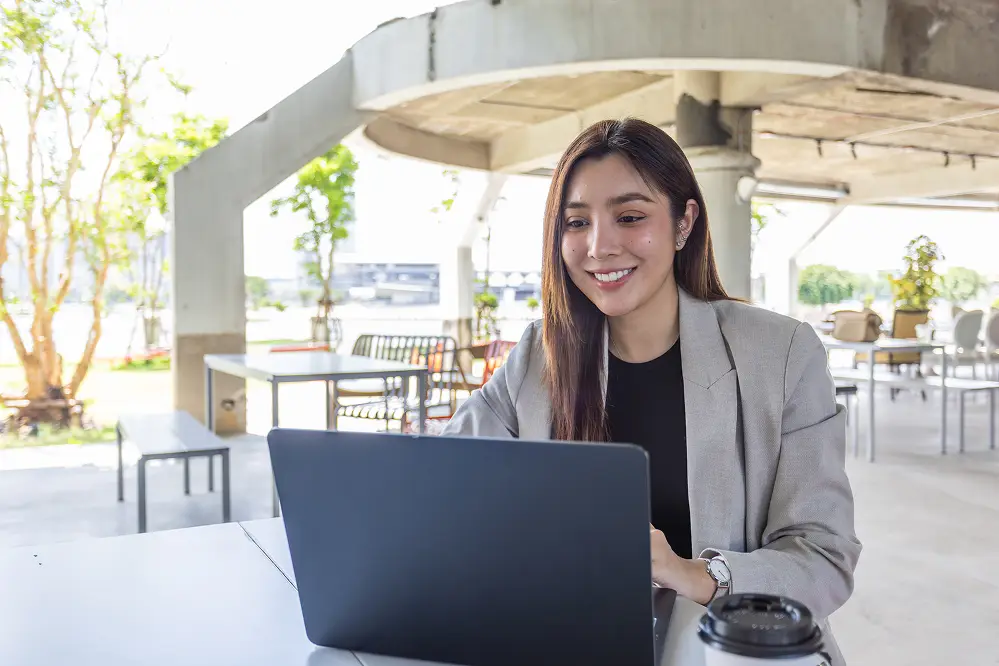 A businesswoman using a laptop at an outdoor patio desk with a coffee cup in the foreground
