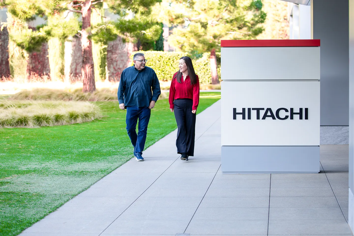 Two colleagues walking together on Hitachi campus near company signage