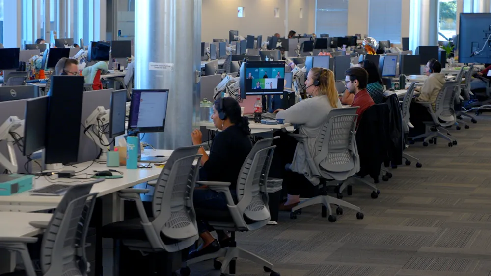 People wearing headsets work at computers in a modern open-plan office.